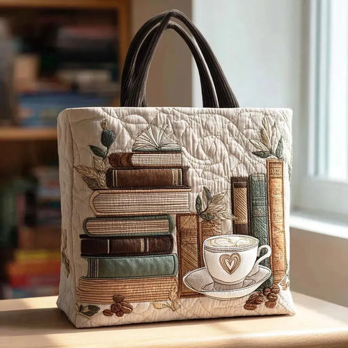 Artisan quilted tote bag with a steaming coffee cup beside an open book and loose turning pages in warm brown tones