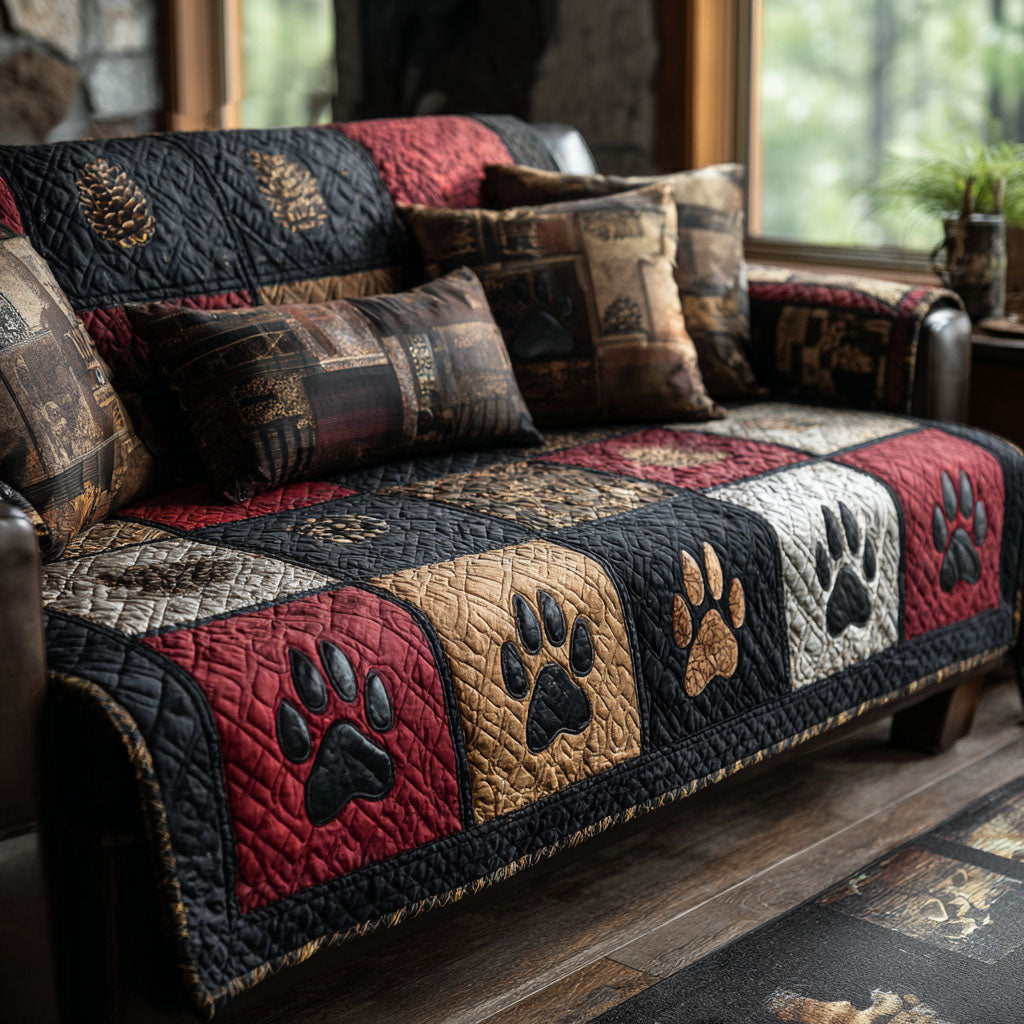 Paw Trail quilted sofa cover with barn red, charcoal, old gold and cream blocks carrying paw prints and pinecone panels