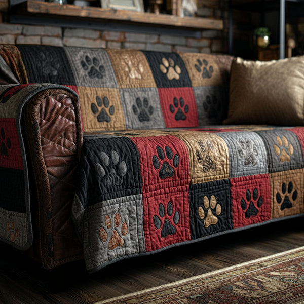 Cabin Paw Patchwork quilted sofa cover with squares of barn red, charcoal, stone grey, tan and gold, each carrying a stitched paw print